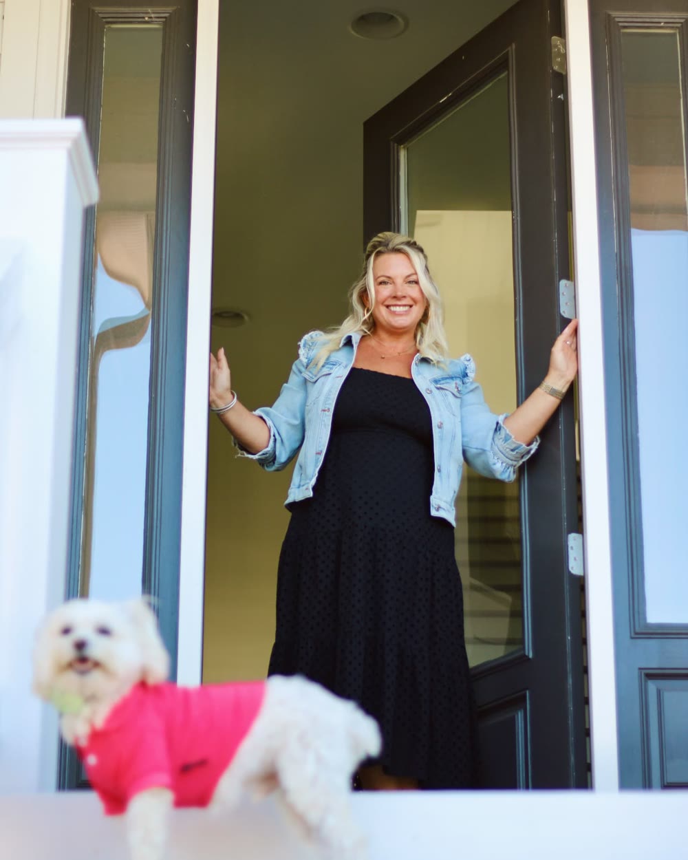 Casey Styers welcoming visitors through the front door of a home, with her dog on the porch step